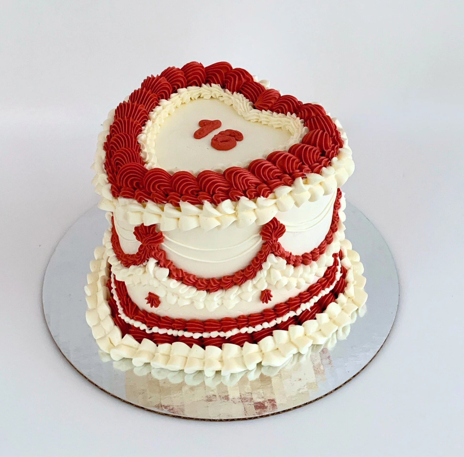 Close up of a custom cake, an 8" heart shaped "lambeth" style cake with extravagant piping in red and white